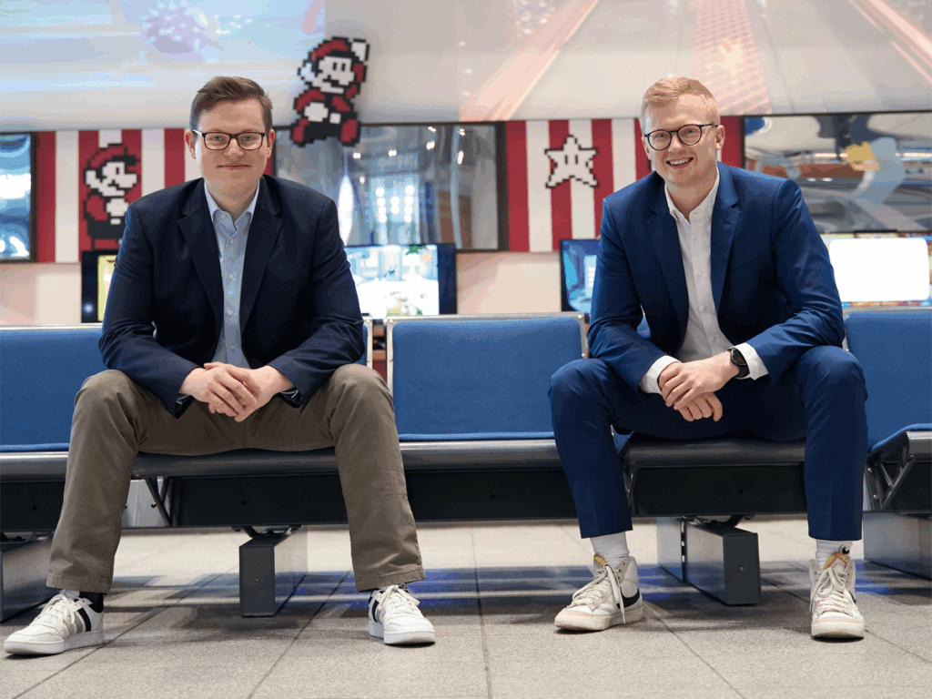 KI-Experten Lukas Güthoff und Nico Rixe im Heinz Nixdorf MuseumsForum, sitzend auf einer blauen Bank