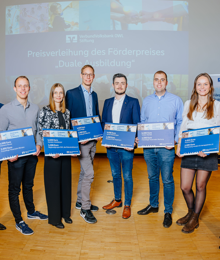 Scheckübergabe bei der Preisverleihung des Förderpreises Duale Ausbildung, sechs junge Menschen stehen mit großen Checks vor einer Leinwand