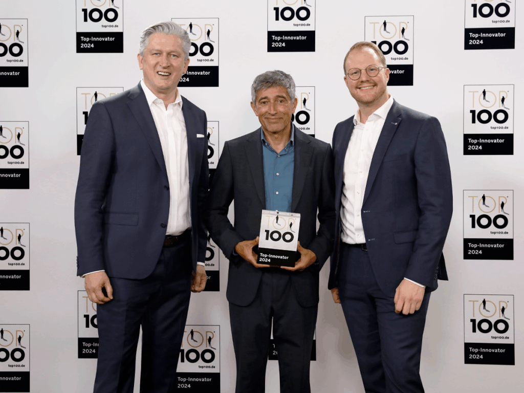 Drei Männer im Anzug, der in der Mitte hält den Preis "Top-Innovator 2024" in den Händen