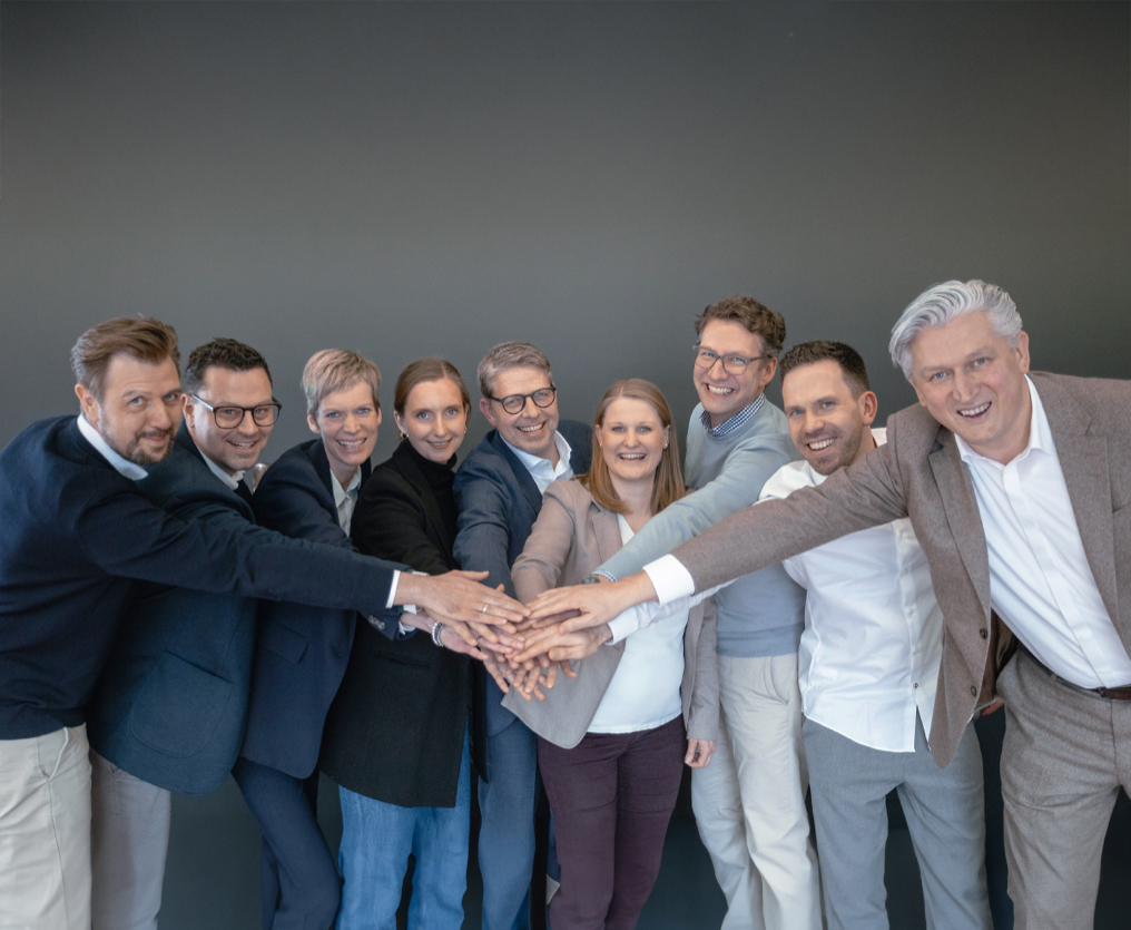 Neun Menschen halten in der Mitte ihre ausgestreckten Hände übereinander